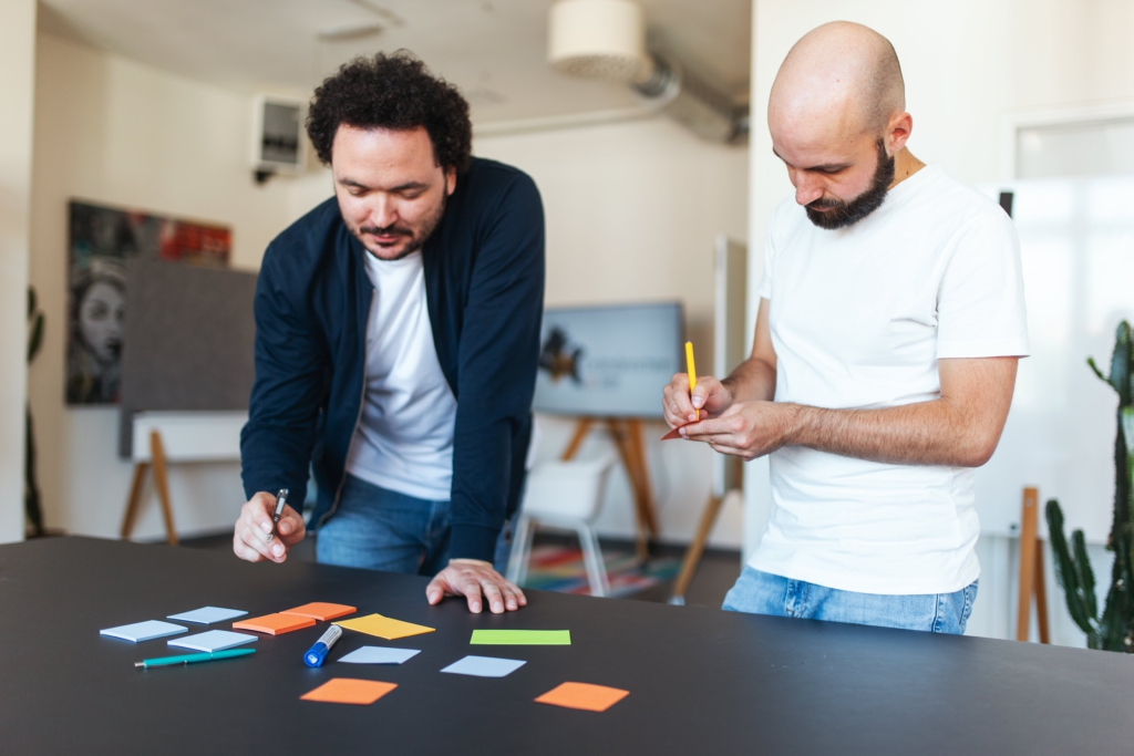 E&B_Brainstorming Sebastian und Felix beim Brainstorm in einem internen Design Thinking Workshop. Beide schreiben auf bunte Zettel und legen diese auf einen Tisch vor sich.