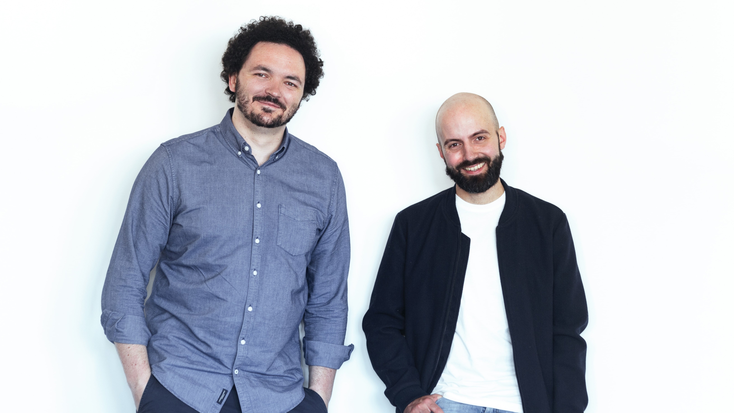 Portrait: Sebastian Jähnke und Felix Bastam. Beide lächeln und schauen in die Kamera. Sebastian trägt ein lockeres Hemd. Felix trägt eine Jacke über einem weisen T-Shirt.
