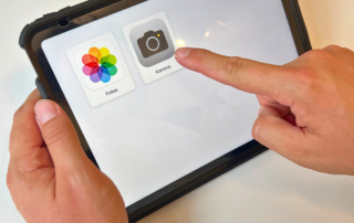 Hand zeigt auf die App-Symbole „Fotos“ und „Kamera“ auf einem iPad-Bildschirm, um die vereinfachte Darstellung des unterstützenden Zugriffs zu demonstrieren.