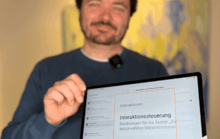 Ein Mann mit lockigen, dunklen Haaren – Sebastian – hält ein Samsung-Tablet in die Kamera. Auf dem Bildschirm ist groß das Wort Interaktionssteuerung zu sehen.
