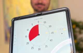 Sebastian hält ein Tablet in die Kamera auf der die TimeTimer-App geöffnet ist. Auf dem Bildschirm ist eine große Uhr.