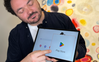 Ein Mann mit kurzen, dunklen, lockigen Haaren und einem dunklen Hemd zeigt auf ein Android-Tablet. Dort ist die Vergrößerung aktiviert und ein Teil des Bildschirms vergrößert.